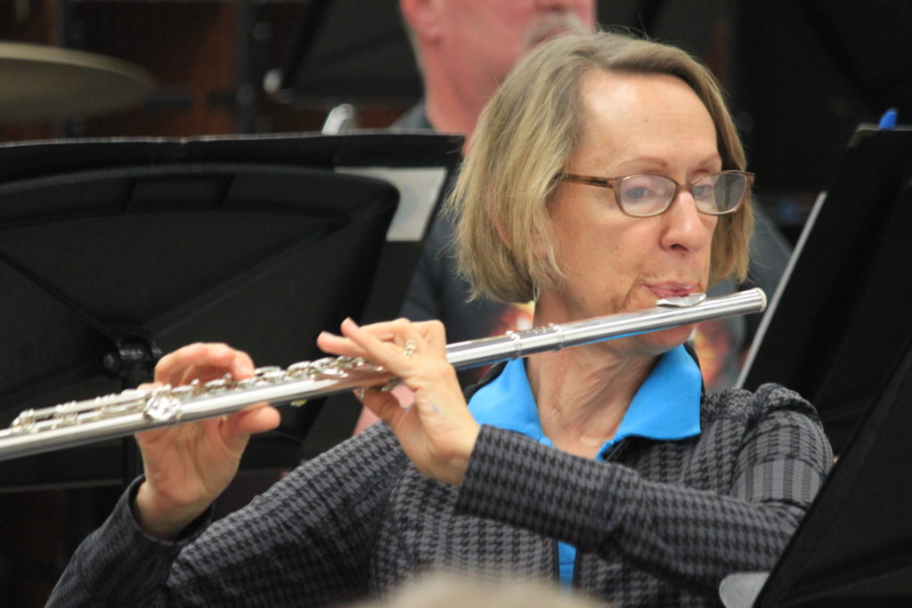 Close up of an older woman with short blonde hair playing the flute during a concert